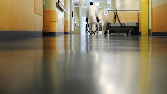 Ein Pfleger schiebt eine Patienten im Rollstuhl über den Klinikflur.