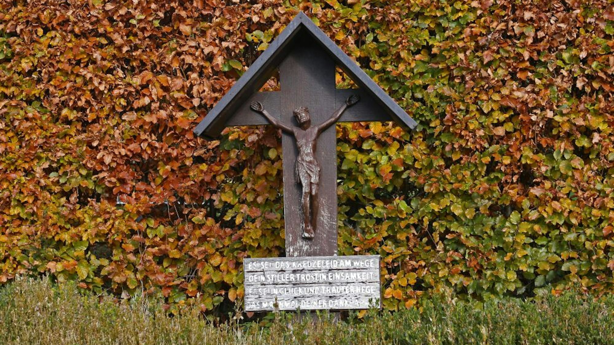 Vor einem Busch hängt eine Jesus-Figur an einem Holzkreuz.