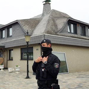 Ein maskierter Polizist steht vor einem Haus