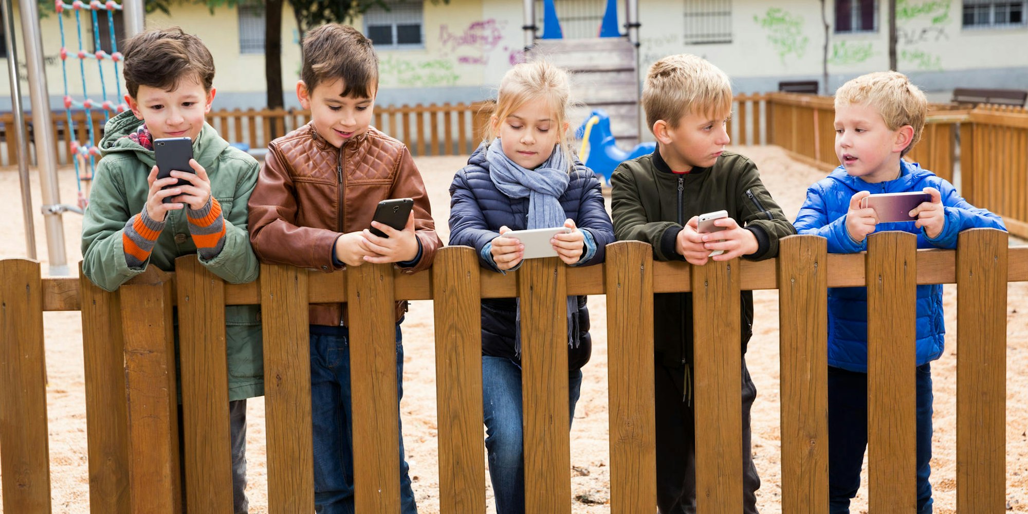 Grundschulkinder stehen mit Handys an einem Zaun.
