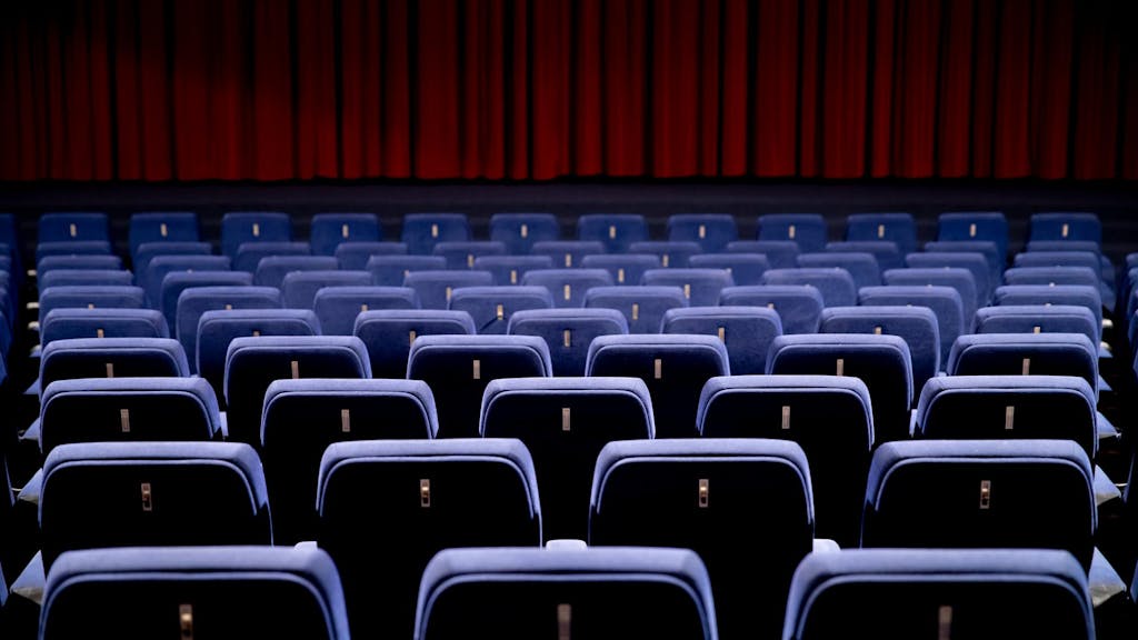 Ein Kinosaal mit Blick über die Sitze auf den geschlossenen Vorhang der Leinwand.