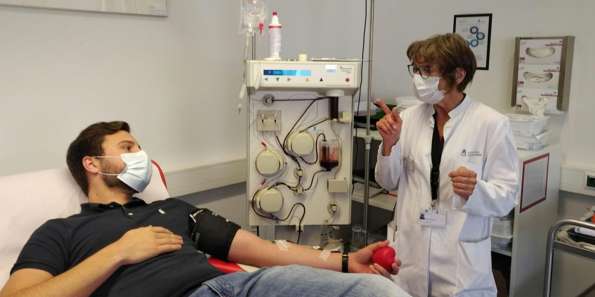 Einer der ersten Spender ist Jan K. Die Mitarbeiterin des Blutspendedienstes am Universitätsklinikum Bonn Heike Brüssler erklärt dem wieder genesenen Covid-19-Patienten den Ablauf der Plasmaspende.